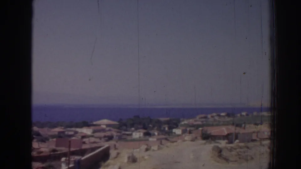 Elevated 1962 Izmir coastal view showing clustered low buildings, a road, sandy terrain, and the sea beyond.