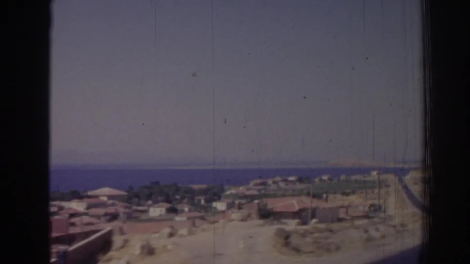 Vintage 8mm frame of Izmir, Turkey, with rooftops and open hillside ground set against a blue sea horizon.
