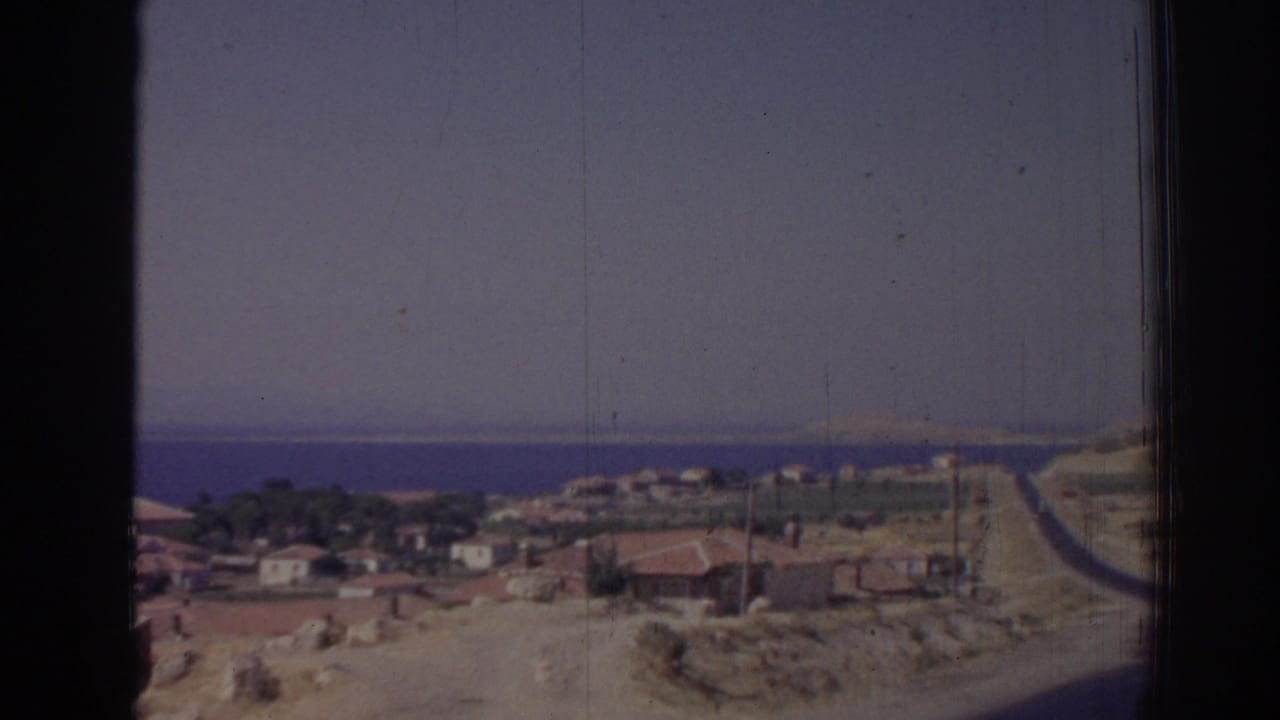 Coastal village road descending toward houses and blue sea.
