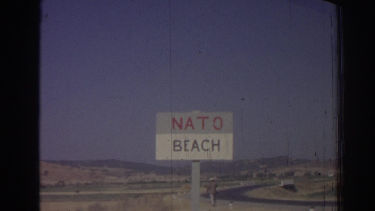Roadside NATO Beach sign against hills and hazy sky.