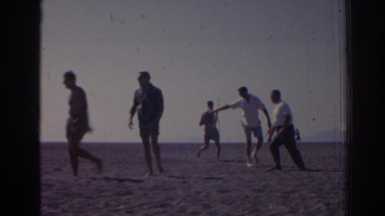 1962 home-movie frame from Izmir, Turkey, showing people walking and playing on a beach beside the sea.