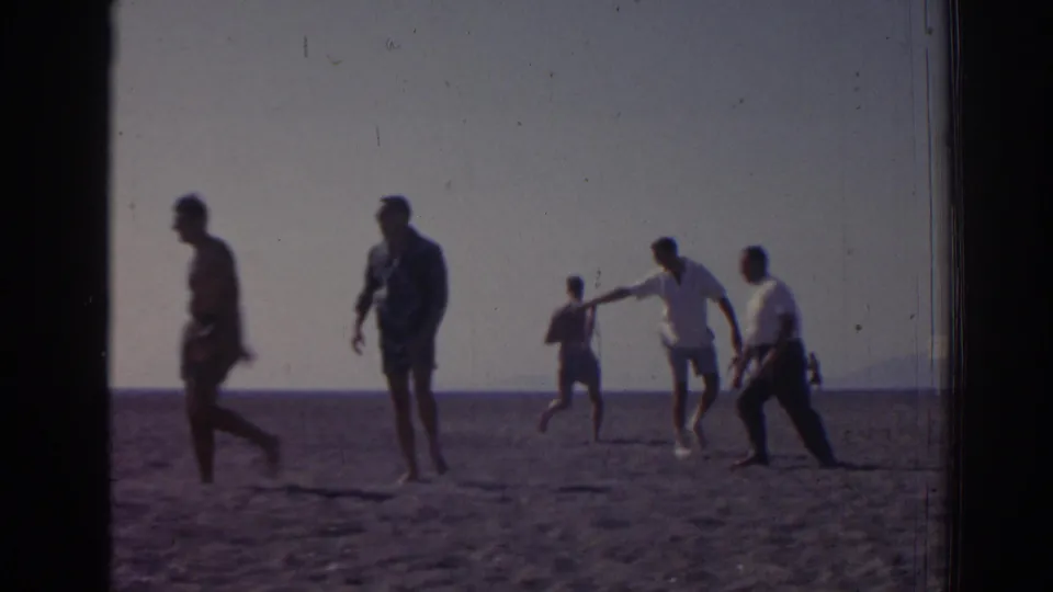 1962 home-movie frame from Izmir, Turkey, showing people walking and playing on a beach beside the sea.