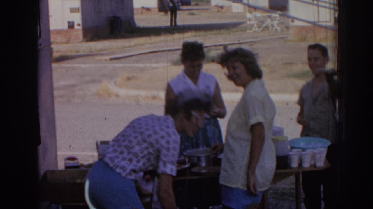 Women stand near an outdoor refreshment table in bright daylight.