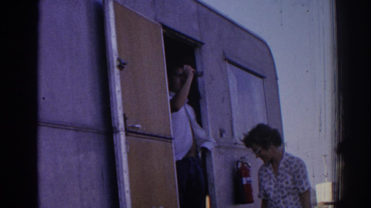 A woman in patterned clothing stands near a trailer doorway in 1962 Izmir footage as a person appears partly inside.