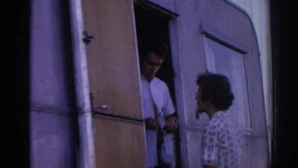 In the trailer doorway, a man in a white shirt faces a woman outside during an informal 1962 Izmir home-movie moment.