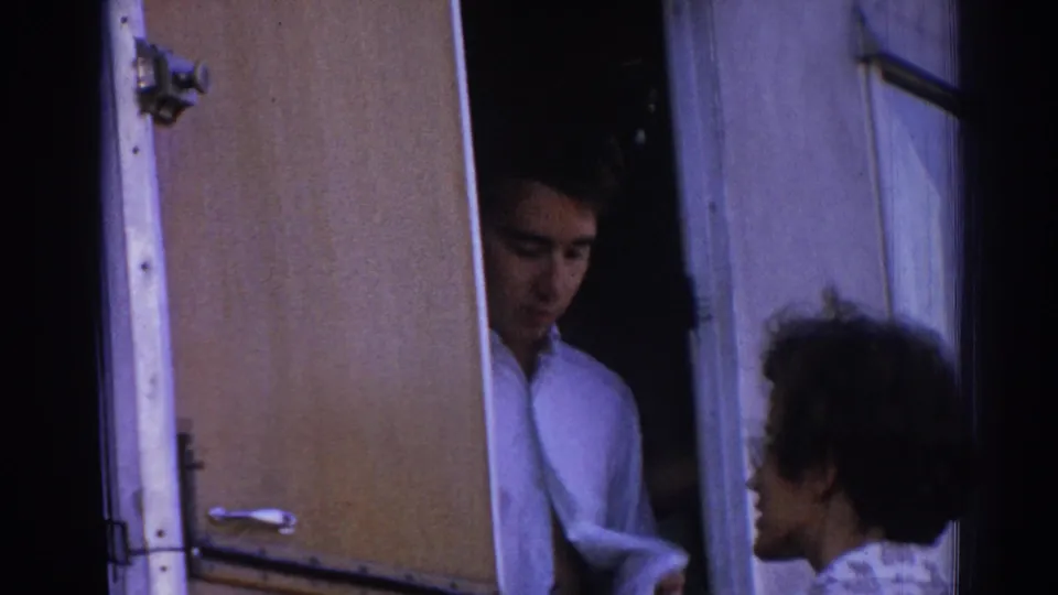 1962 Izmir home-movie frame showing a man in a white shirt at a camper doorway speaking with a woman outside.