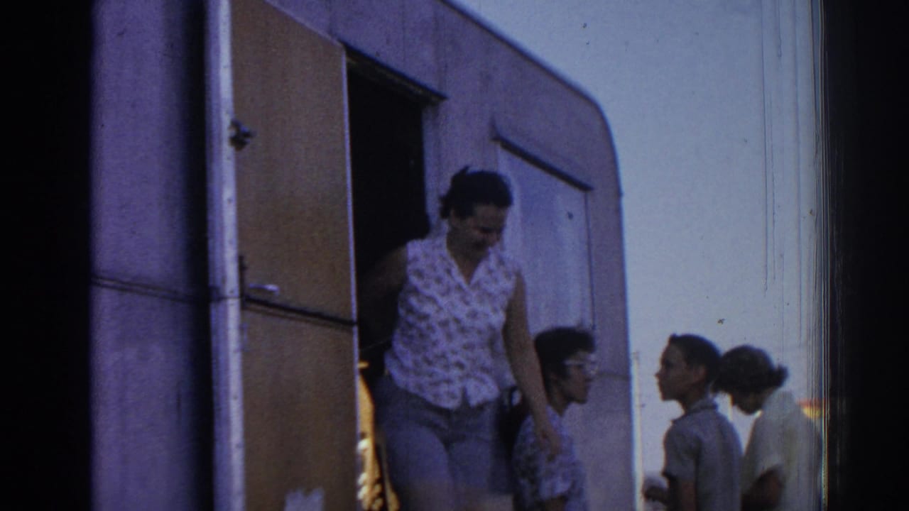 Woman steps down from a camper while several adults stand nearby.
