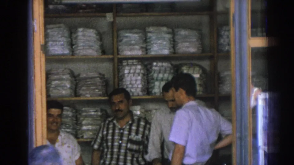 Near the end of the 1962 Izmir shop shot, several men gather by the storefront as stacked wrapped goods line the shelves behind them.