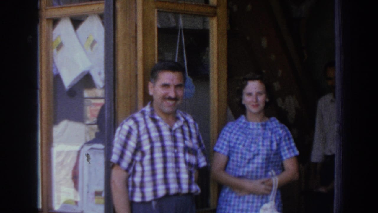 Man and woman smiling outside a shop window with papers displayed behind them.