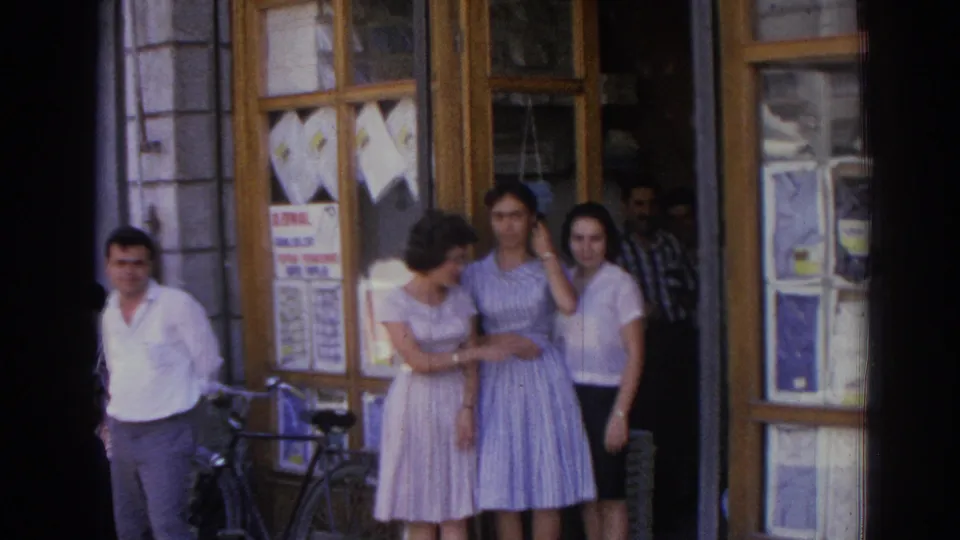 In the Izmir street scene, the women remain outside the shop while one adjusts her hair and a bicycle is parked near the doorway.