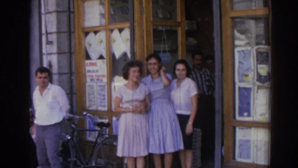The 1962 Izmir home-movie frame shows three women posed by a shop entrance with men nearby and a bicycle at the curb.