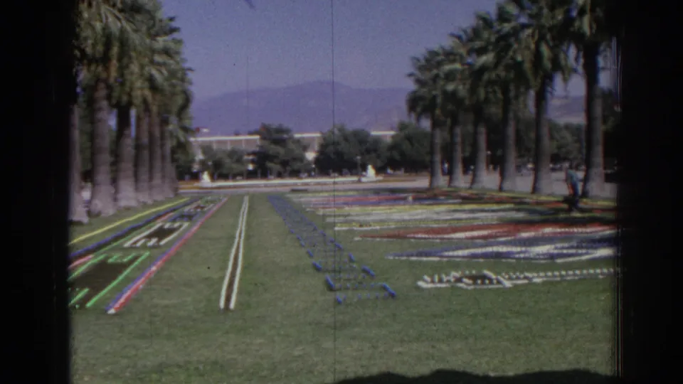 1962 Izmir frame showing palm-lined grounds, colorful planted designs, open lawn, and distant hills in soft 8mm color.