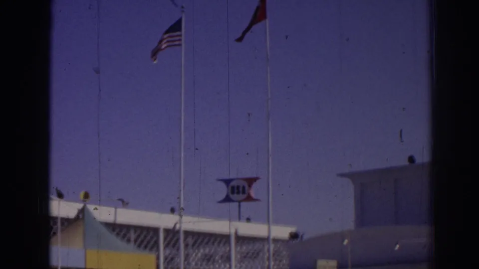 1962 Izmir 8mm view of flags, a USA sign, and geometric venue details from behind a dark frame edge.