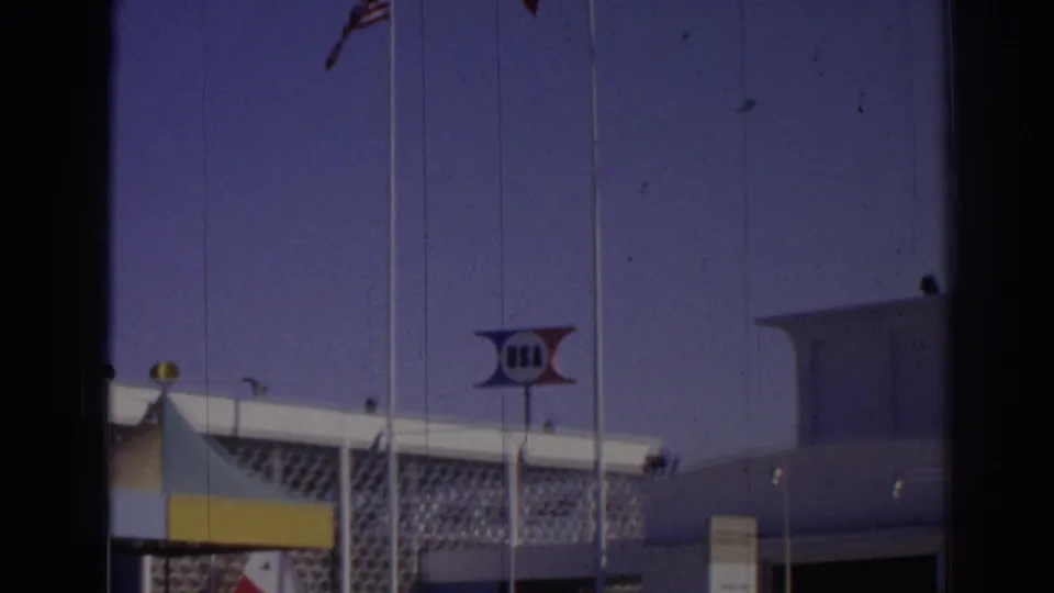 1962 Izmir frame showing U.S. and Turkish flags beside a white venue building with a USA sign.