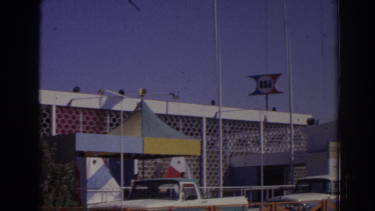 1962 Izmir frame with the apparent USA sign above a mid-century building facade, a striped canopy, railings, and several parked cars.