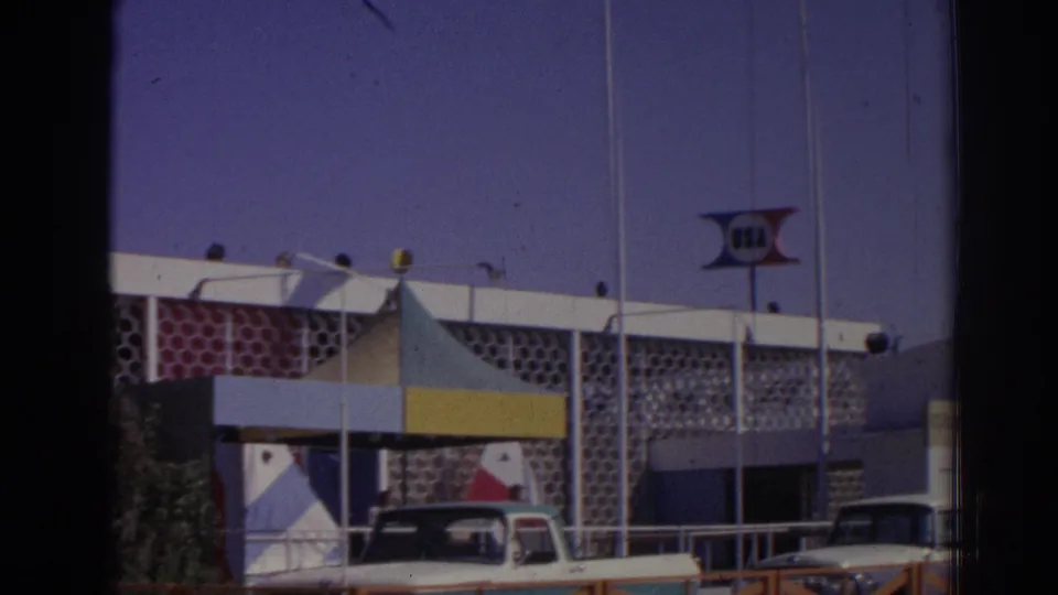 1962 Izmir frame with the apparent USA sign above a mid-century building facade, a striped canopy, railings, and several parked cars.