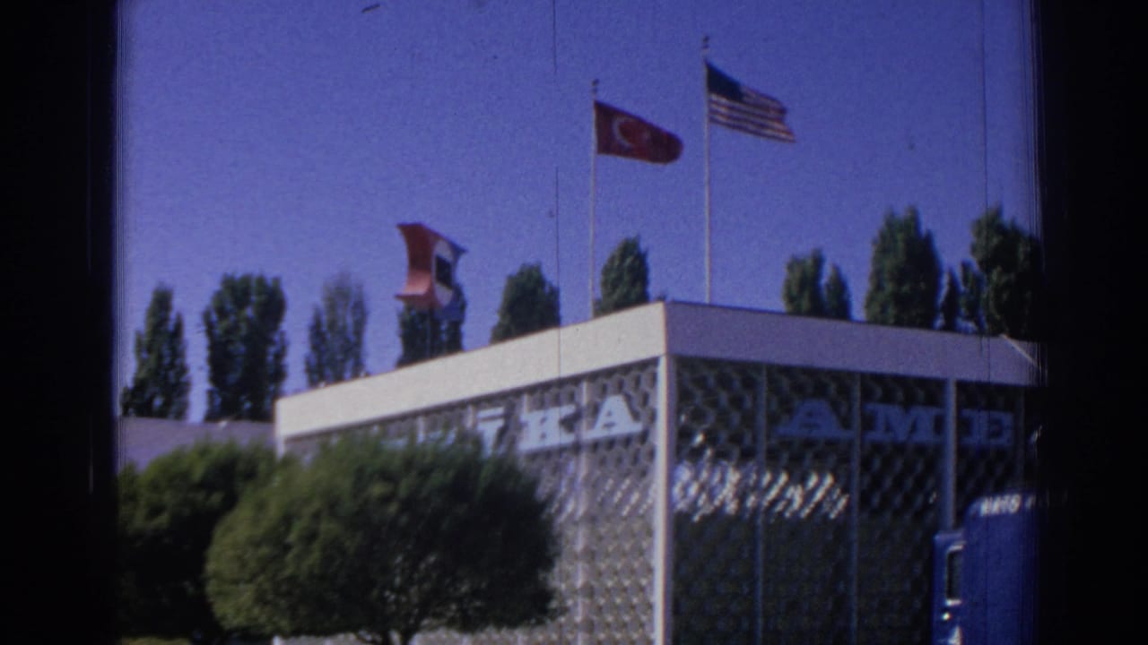 Turkish and U.S. flags above a patterned NATO building under a blue sky.