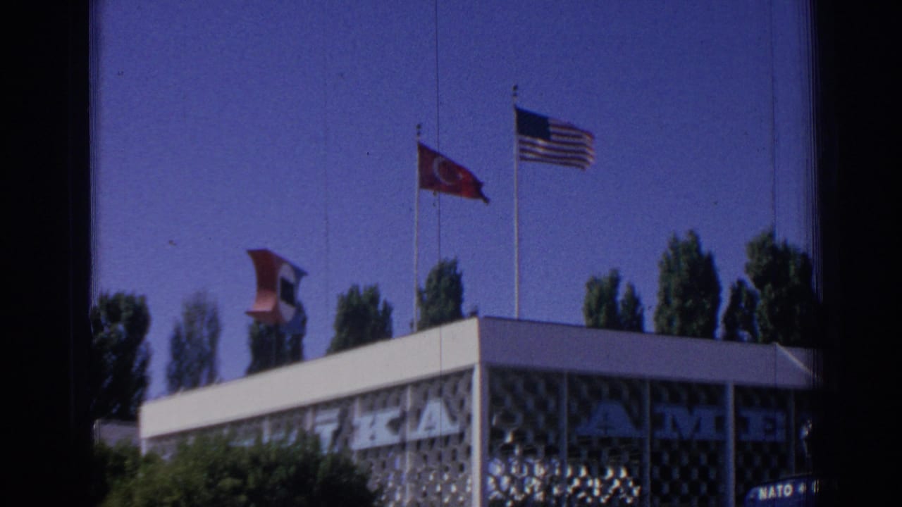 Turkish and U.S. flags fly above a NATO facade with trees in the background.