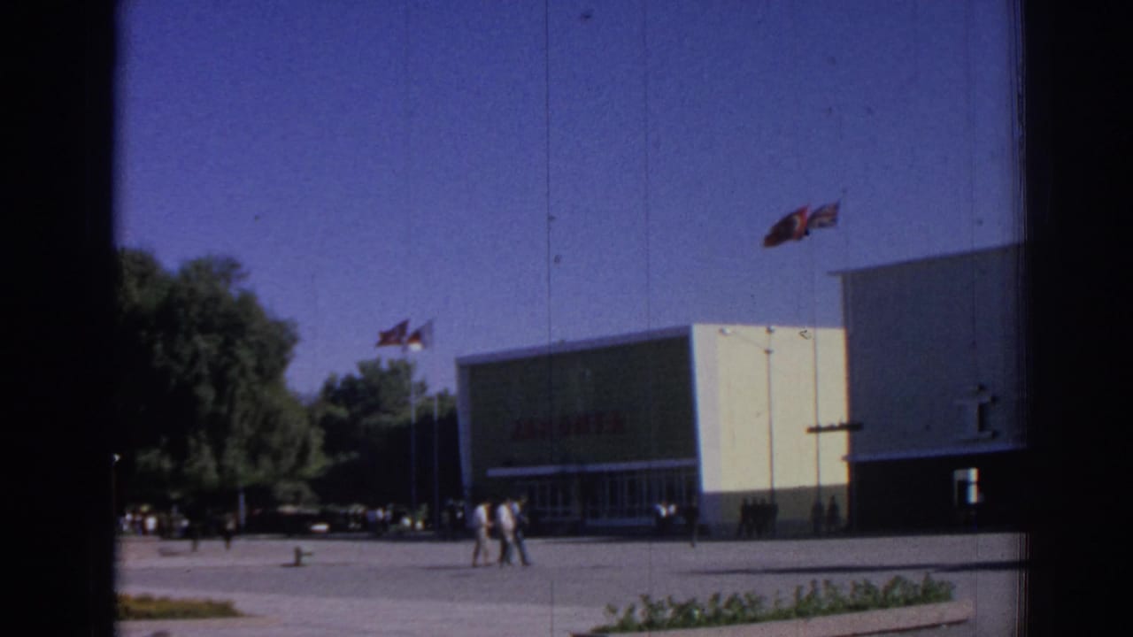 Modern building with JAPONTA sign, flags, pedestrians, trees, and plaza paving.