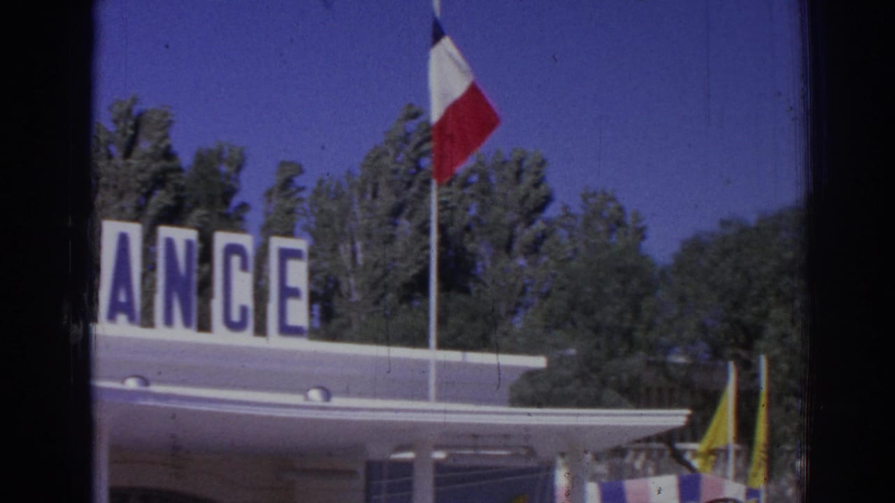 Partial FRANCE sign, French flag, pavilion roof, and trees during a rightward pan.