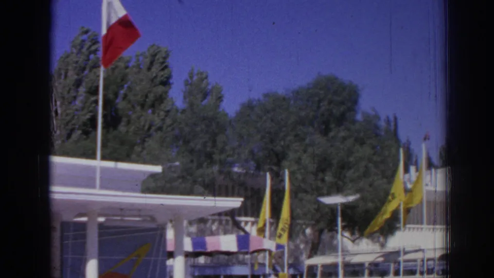 1962 Izmir fairground view with the French flag at left, yellow flags, trees, pavilion structures, and parked buses.