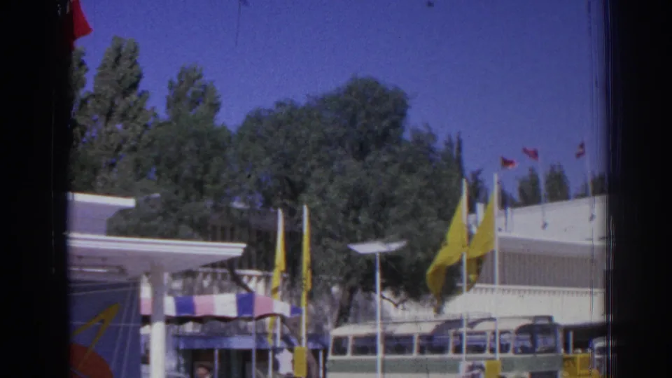 End of the pan across the Izmir fairground area, showing yellow flags, trees, buses, and adjacent exhibition buildings.