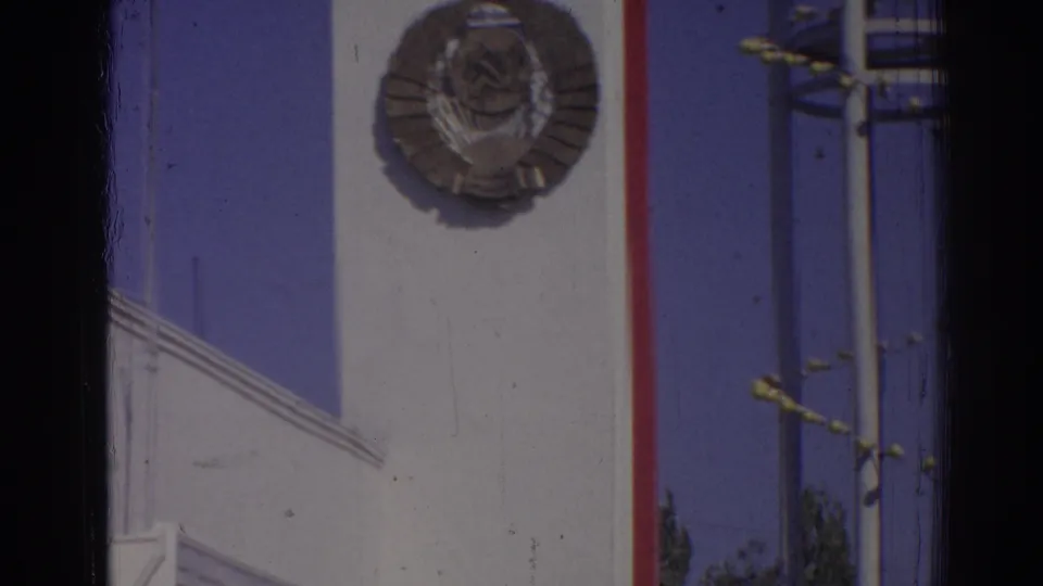 1962 Izmir facade view centered on a large circular Soviet-style emblem beside red trim and blue sky.