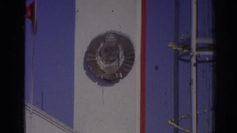 1962 Izmir close facade view showing the large Soviet-style circular emblem, red vertical trim, poles, and blue sky.