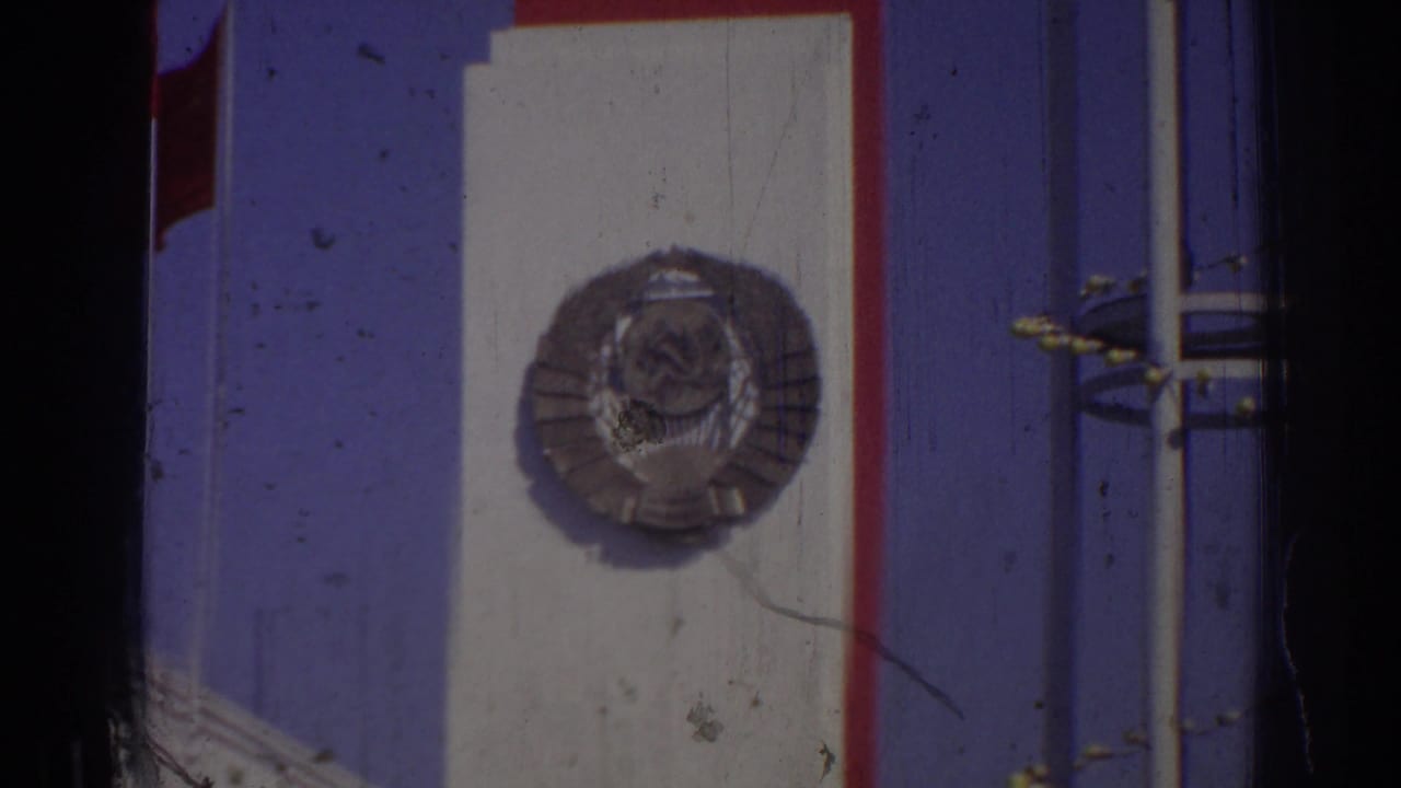 Close view of a blue sign area with a white panel, circular Soviet-style emblem, red trim, poles, and a Turkish flag edge.