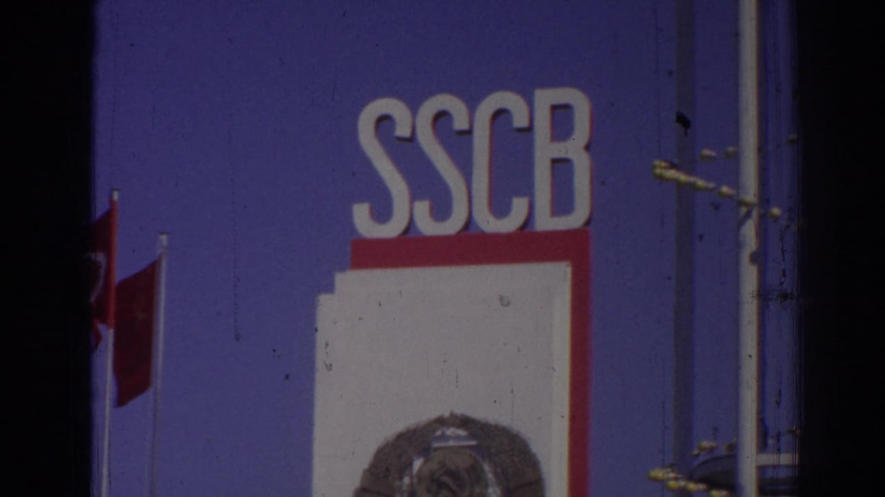 Blue sign with large white SSCB letters, red-and-white panel below, circular emblem, poles, and a Turkish flag.