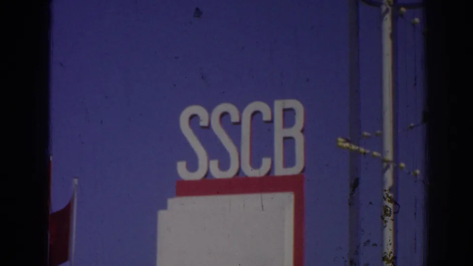 1962 Izmir 8mm frame emphasizing large SSCB letters on a blue sign surface, with red-and-white paneling, metal poles, and a Turkish flag edge.