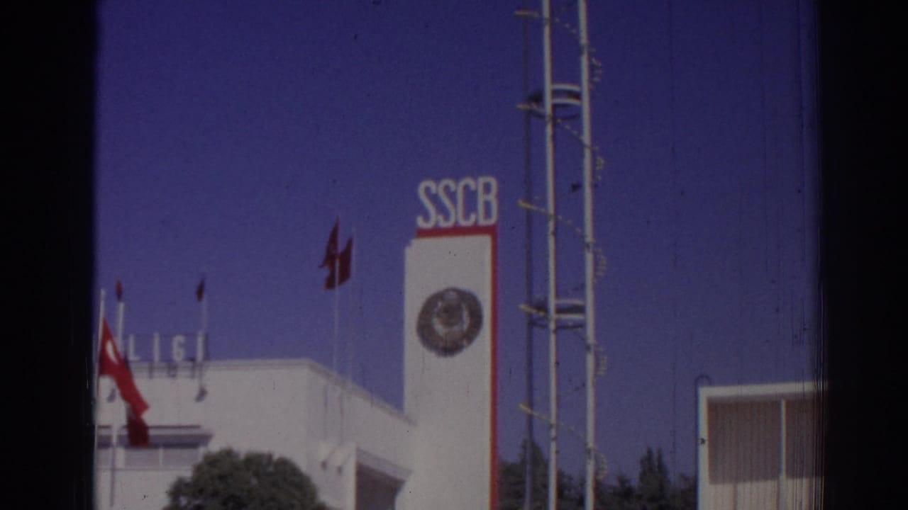 1962 Izmir exterior with SSCB lettering, a circular emblem, red flags, antenna-like structure, and part of a modern building.