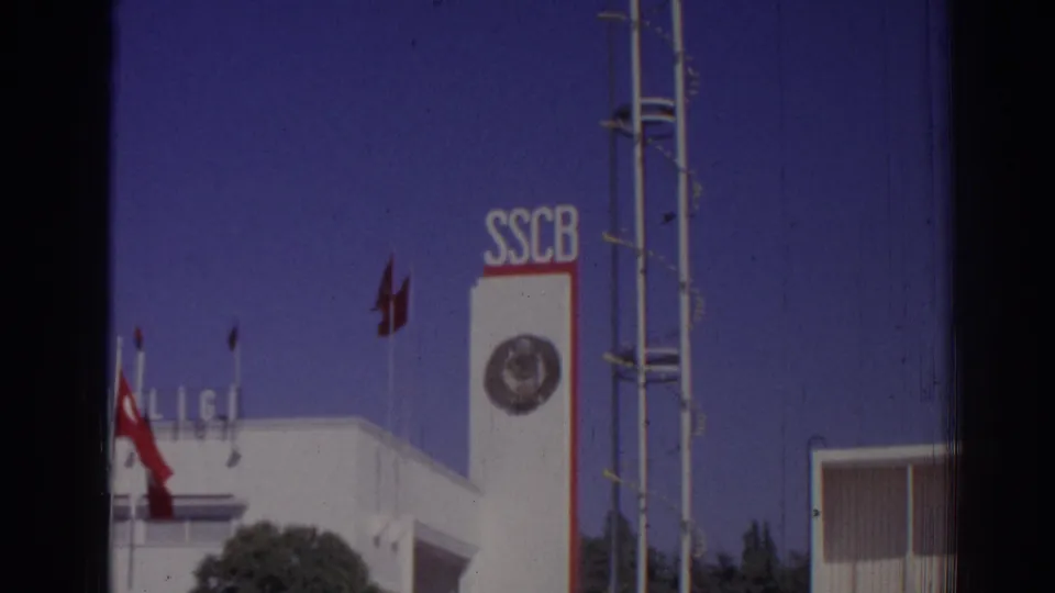 1962 Izmir exterior with SSCB lettering, a circular emblem, red flags, antenna-like structure, and part of a modern building.