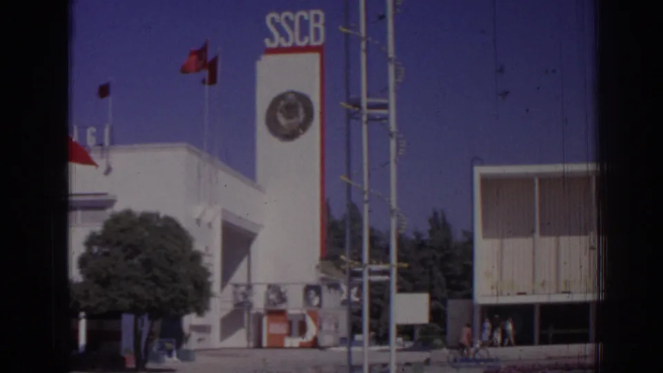 1962 Izmir street-level view of the SSCB-marked white tower with flags, tree, entrance details, and neighboring modern facade.