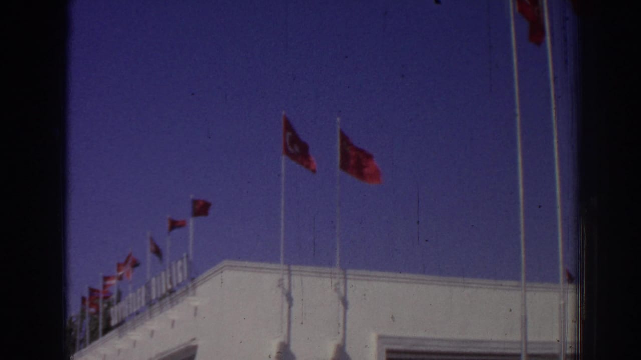 Rows of red flags line the roof of a white building beneath a blue sky.