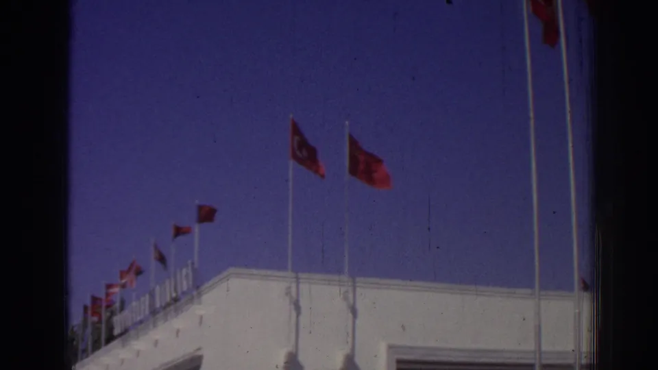 1962 Izmir frame with multiple Turkish flags along a white rooftop, seen from a low exterior angle.