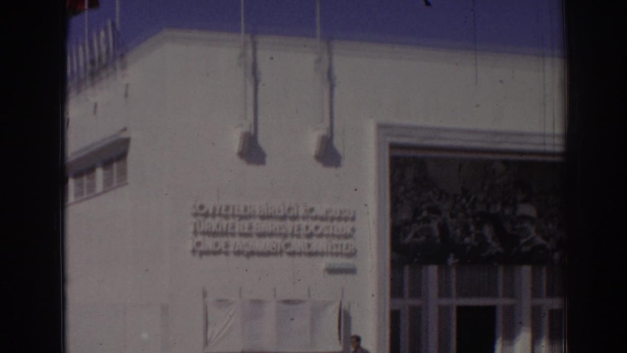 Closer view of the white facade with flagpoles, inscription, and a large doorway.