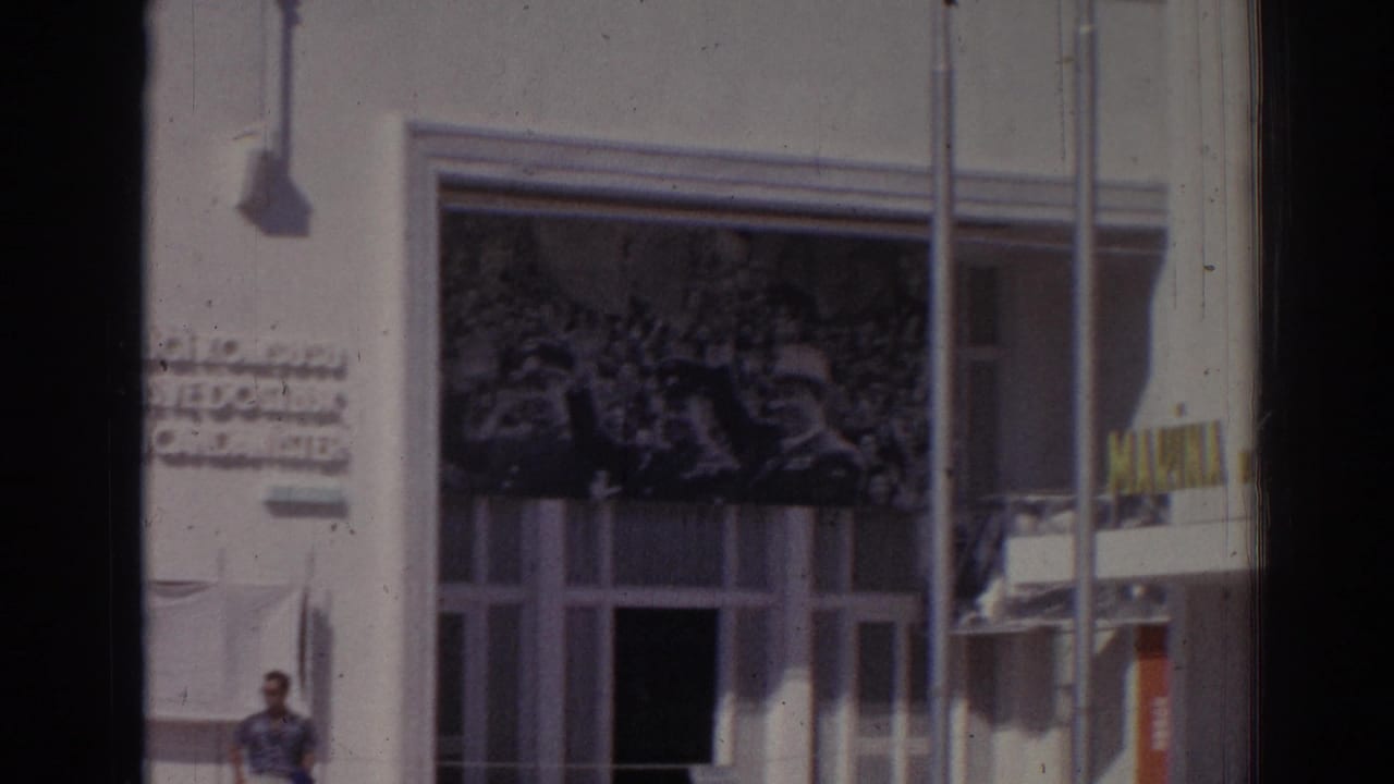 White building facade with a large crowd mural above windows and a man walking at lower left.