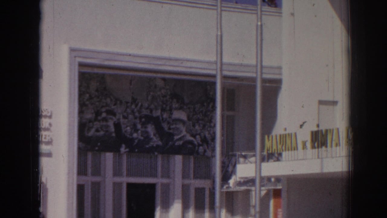 White facade with crowd mural, vertical poles, windows, and yellow lettering at the right edge.