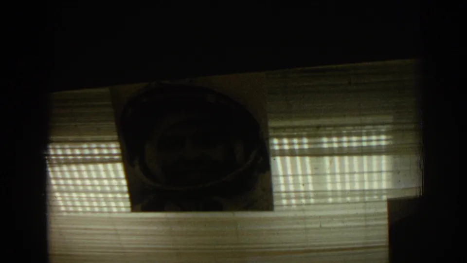 1962 Izmir frame showing a framed portrait of a helmeted man behind horizontal blinds in a dim display window.
