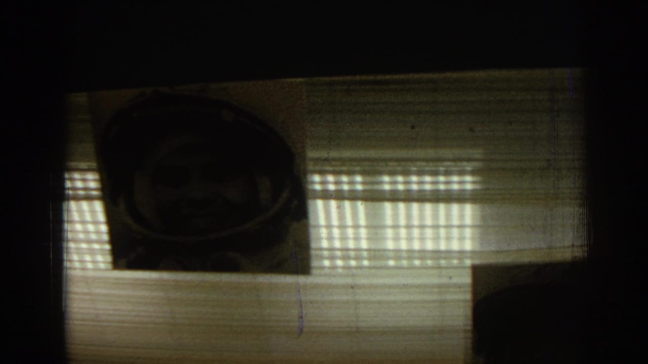 Dark overhead view of a framed astronaut portrait hanging near striped light and ceiling blinds.
