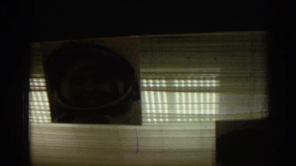 1962 Izmir home-movie frame showing a dim ceiling view with a hanging astronaut portrait and striped light patterns.