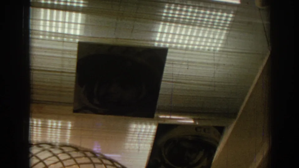 1962 8mm frame showing multiple astronaut portraits hanging in a museum-like interior in Izmir, with a wire light fixture below.