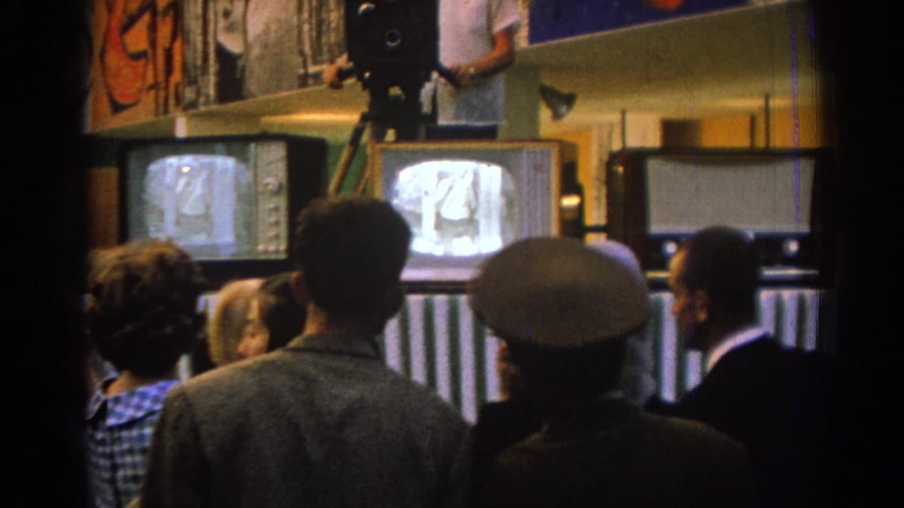 Crowd seen from behind watching CRT televisions beneath a tripod-mounted camera.