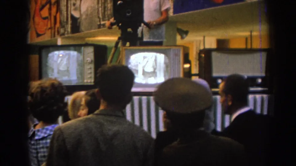 In Izmir, Turkey in 1962, people stand indoors watching CRT televisions while a camera operator works above the screens.