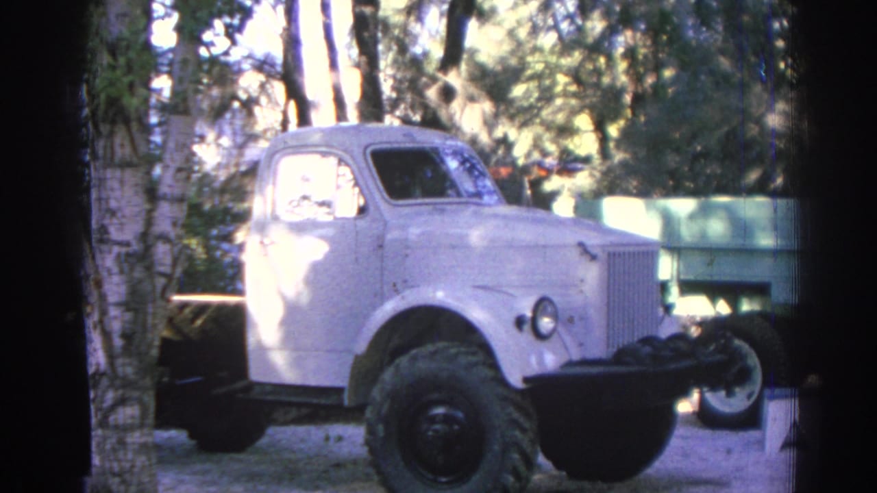 Pale vintage truck parked outdoors near trees and a low wall.