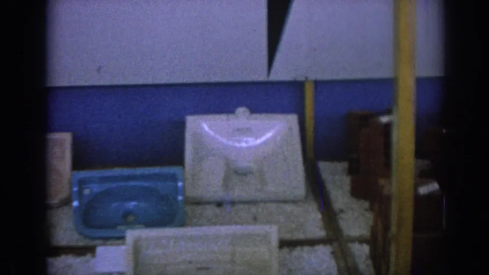 1962 Izmir 8mm frame showing a white porcelain sink basin beside a blue basin on a display surface against blue and white wall panels.
