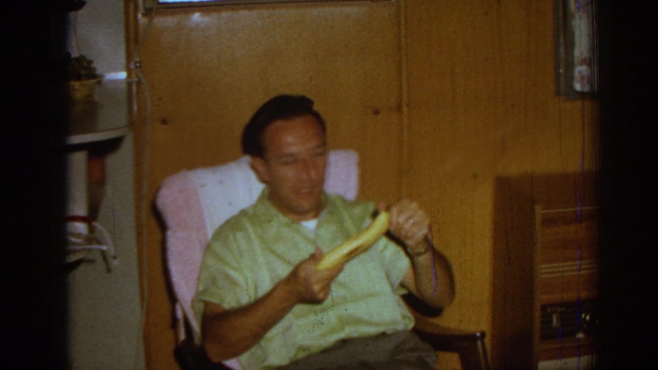 Man looks down while handling a banana in a wood-paneled interior.