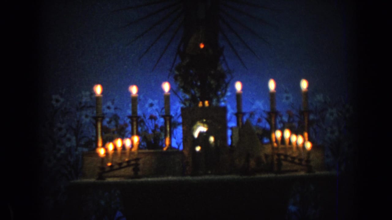 Candlelit religious statue before a blue backdrop inside a dark church interior.