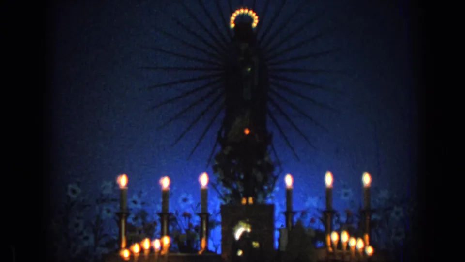 1962 Izmir church footage showing a haloed religious statue rising behind tall candles and warm votive lights.